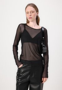 Svart genomskinlig långärmad topp med rundad halsringning, lager på en svart bralette. Kombinationen med svarta läderbyxor och en liten lackväska.