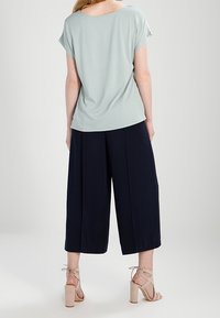 Blusa corta de manga corta en verde claro combinada con pantalones anchos de tiro alto en azul marino y tacones beige con tiras. Tela suave y corte relajado.