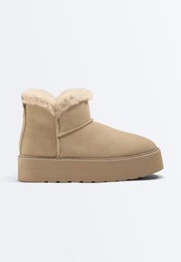 Bottine beige en daim avec une semelle épaisse et une doublure en shearling duveteuse repliée sur le bord supérieur.