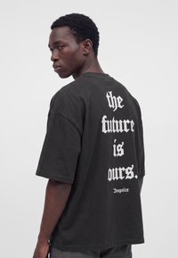 Jeune homme portant un t-shirt noir avec un texte blanc dans le dos disant « the future is ours. » et « Dropsize » en dessous.
