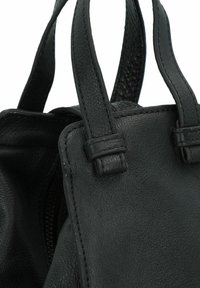 Bolso de mano de cuero negro con superficie texturizada, dos asas cortas y costuras visibles a lo largo de los bordes. Detalle de cremallera parcialmente expuesto.