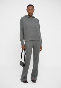 Felpa grigia con cappuccio e maniche lunghe, abbinata a pantaloni grigi. Texture liscia, vestibilità rilassata, accessoriate con una piccola borsa nera.