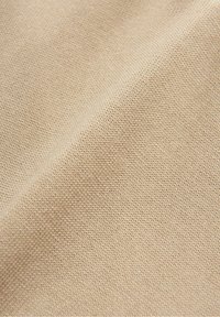 Gros plan sur un tissu beige montrant une texture de maille fine et de légères ombres de plis.