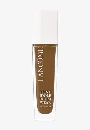 Lancôme Teint Idole Ultra Wear Foundation in einer klaren Glasflasche mit einem weißen Deckel. Die Farbe ist tiefbraun. Auf der Flasche steht der Produktname.