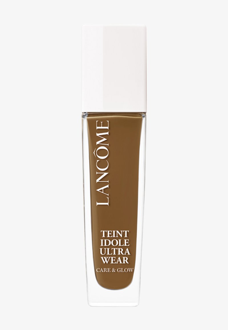Lancôme Teint Idole Ultra Wear foundation i en klar glassflaske med hvit kork. Fargen er dyp brun. Teksten på flasken angir produktnavnet.
