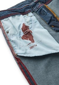 Denim teksad sinise ja helesinise kangaga, kontrastsete punaste tikanditega ja trükitud graafikuga taskul. Omab metallist detaile.