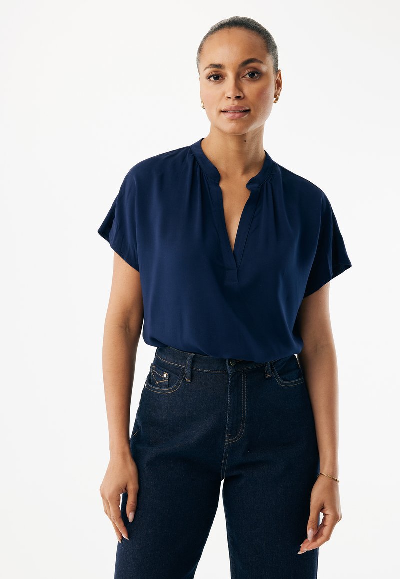 Marineblaue Bluse mit kurzen, aufgekrempelten Ärmeln und einem knopflosen V-Ausschnitt. Hergestellt aus leichtem Stoff, hat sie eine glatte Textur und einen dezenten Fall.