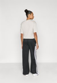 Krajša svetlo siva majica, kombinirana s črnimi širokimi hlačami z belimi črtami ob straneh. Tekstura je videti gladka.