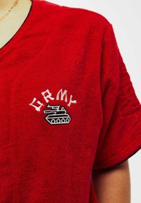 Camicia in terry rossa con maniche corte, caratterizzata da testo bianco "ARMY" e un grafico di una canotta nera ricamato sul davanti.