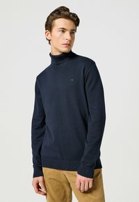 Granatowy sweter z golfem z miękkiej dzianiny, z prążkowanymi mankietami i dołem, z małym logo po lewej stronie klatki piersiowej.