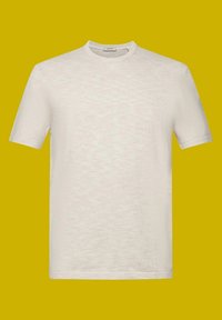 T-shirt blanc à manches courtes avec un col rond, présentant un tissu texturé et une coupe décontractée, exposé sur un fond jaune.