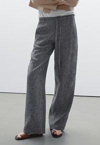 Grey, wide-leg trousers made from textured fabric, featuring a tie belt and a relaxed fit. Paired with black flat sandals.