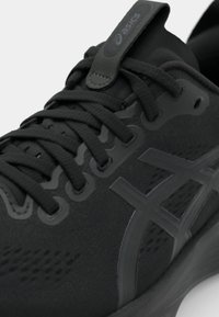 Chaussure de sport noire avec un dessus texturé, un bout rond et une semelle extérieure texturée. Dotée de lacets ton sur ton et d'un logo ASICS sur la languette.