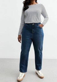 Jeans in denim blu a vita alta con gamba dritta, abbinati a una maglietta a maniche lunghe bianca e nera a righe e scarpe da ginnastica bianche.