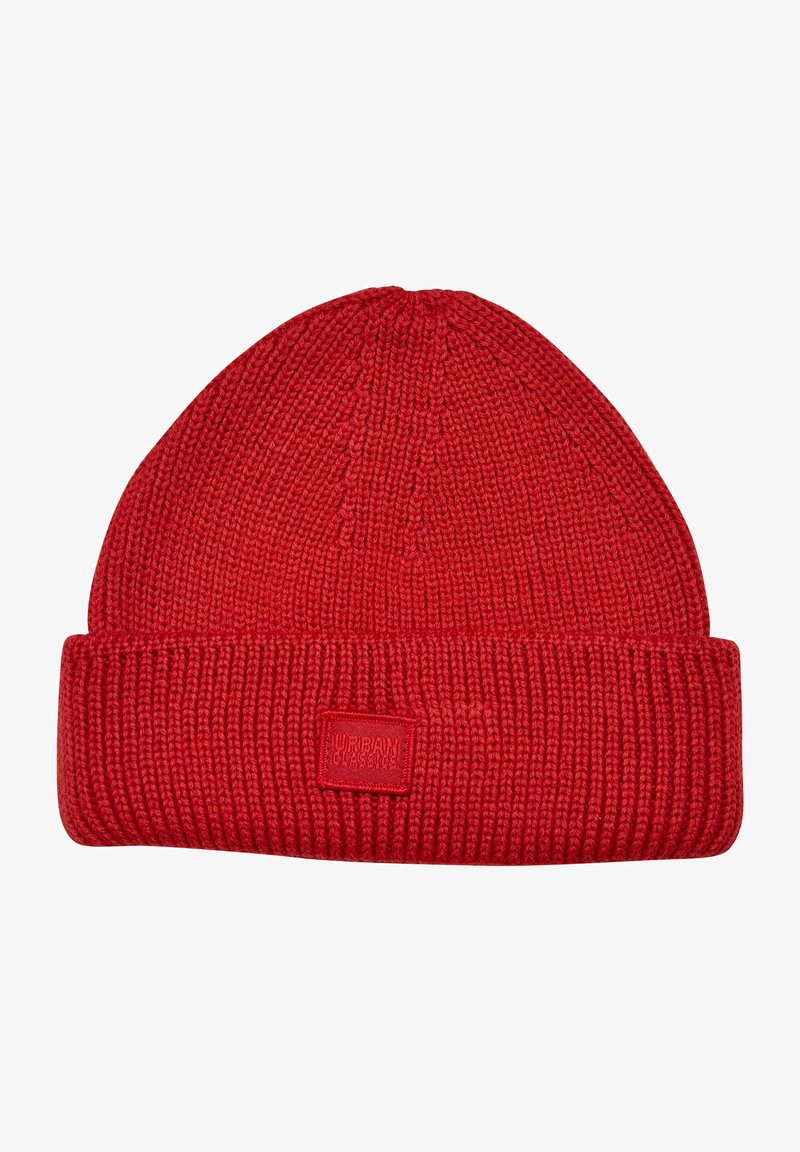 Red knitted beanie hat with a ribbed texture, fold-over cuff, and a small square logo patch. Simple, unadorned design.