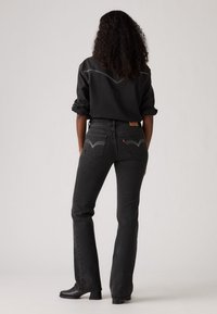Sorte denim jeans med en flared design, der har kontrasterende syninger og karakteristiske baglommer. Parret med en matchende sort skjorte.