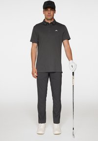 Grå piké med krage, ihop med grå byxor. Vita handskar på vänsterhanden, håller en golfklubba. Vita sneakers fulländar outfiten.