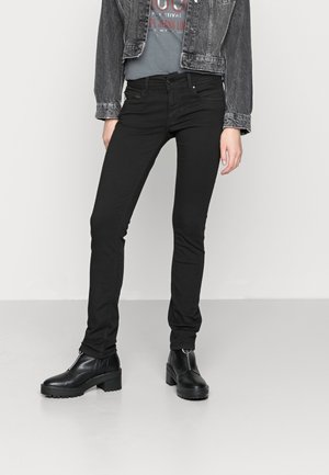 Personne portant un jean slim noir, des bottines noires à talons carrés, un t-shirt bleu délavé à motif graphique et une veste en jean noire courte.