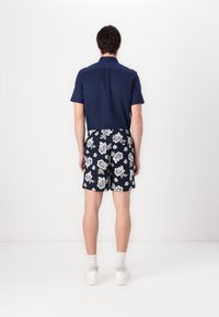Kortermet marineblå skjorte kombinert med knelange svarte shorts med hvite blomster mønster. Modellen har på seg hvite joggesko og ankelstrømper.