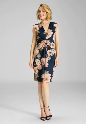 Sukienka w kwiaty w kolorze granatowym, z głębokim dekoltem w kształcie litery V i skręconym przodem. Posiada krótkie rękawy i długość do kolan.