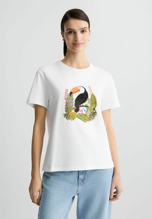 Hvid kortærmet t-shirt med et farverigt tukan omgivet af grønne planter og blomster, lavet af bomuld med en afslappet pasform.
