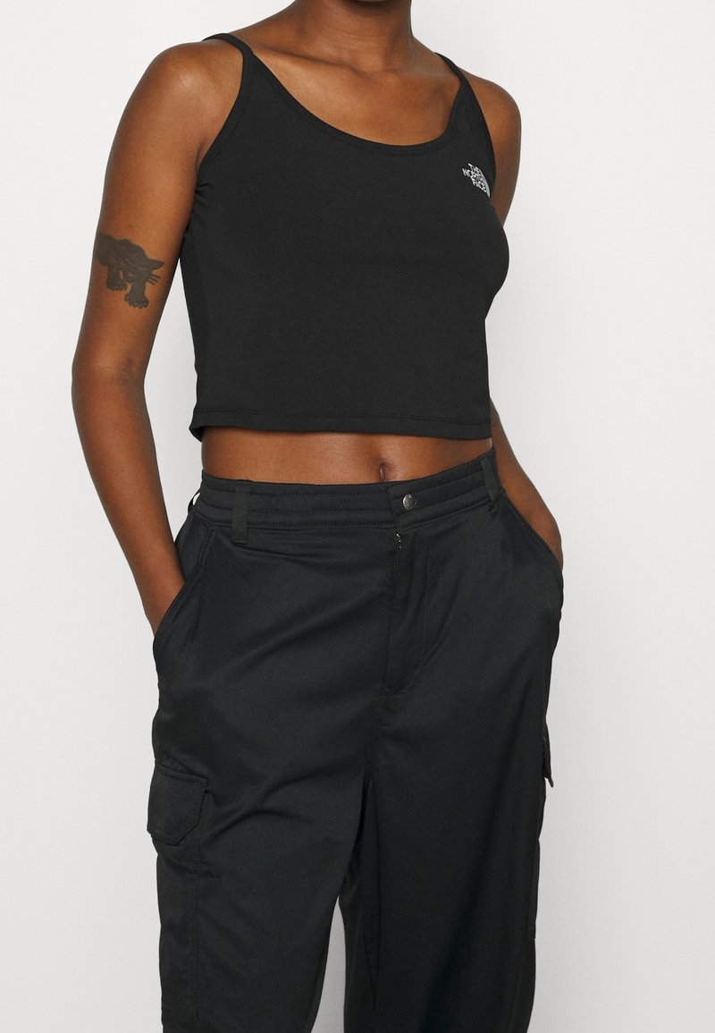 Top corto negro sin mangas con tirantes finos y un logo en el lado izquierdo del pecho; combinado con pantalones cargo negros a juego que cuentan con bolsillos laterales.