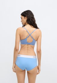 Braletă bleu deschis cu bretele reglabile, cu un design decupat pe spate. Chiloți bleu deschis cu talie înaltă și bandă albă Calvin Klein în talie.