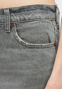 Szare dżinsy z przetarciem na krawędzi kieszeni, miedziane elementy i klasyczny pięć kieszeniowy design. Teksturowany, miękki materiał.