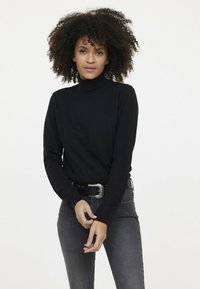 Pull en col roulé noir en tissu tricoté doux, avec des manches longues et une coupe ajustée, associé à un jean gris et une ceinture noire.
