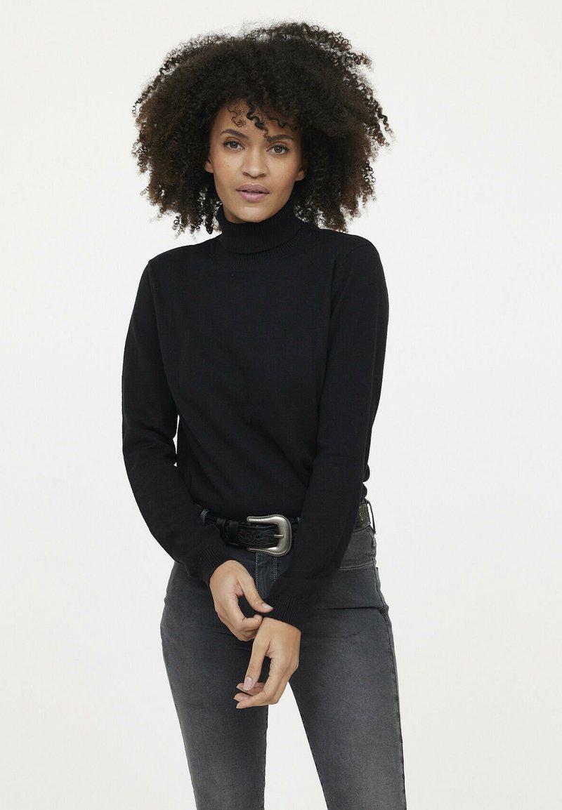 Pull en col roulé noir en tissu tricoté doux, avec des manches longues et une coupe ajustée, associé à un jean gris et une ceinture noire.