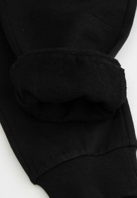 Szczegół czarnej bluzy z miękkim, teksturowanym mankietem i ryflowanym dołem. Materiał wydaje się elastyczny, a jego powierzchnia jest gładka ogólnie.