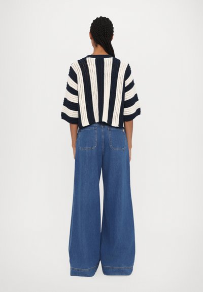 Pulover croșetat cu dungi albastre și albe, cu mâneci scurte, asociat cu blugi din denim cu picioare largi în nuanțe de albastru deschis. Design curat și material texturat.