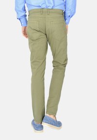 Pantaloni verde oliva con una vestibilità affusolata, dotati di tasche posteriori con dettagli di cucitura, abbinati a scarpe blu senza lacci.
