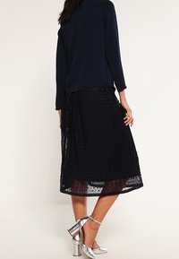 Maglietta a maniche lunghe blu marina abbinata a una gonna midi nera plissettata. La gonna presenta un design strutturato, strati semi-trasparenti e scarpe con tacco alto metalliche.