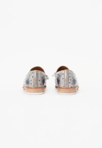 Chaussures en cuir argenté avec un design perforé, ornées de petits clous et d'une semelle en bois brun clair. Comprend un détail de lacet à l'arrière.