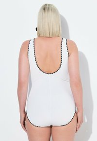 Maillot de bain blanc avec un dos décolleté, bord noir en forme de coquille le long des bords et texture côtelée. Le design offre une silhouette ajustée.