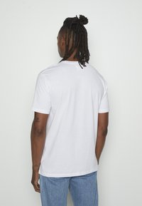 Vit bomullströja med korta ärmar, rund halsringning och rak nederkant. Bakvy som visar en enfärgad design och slät textur.