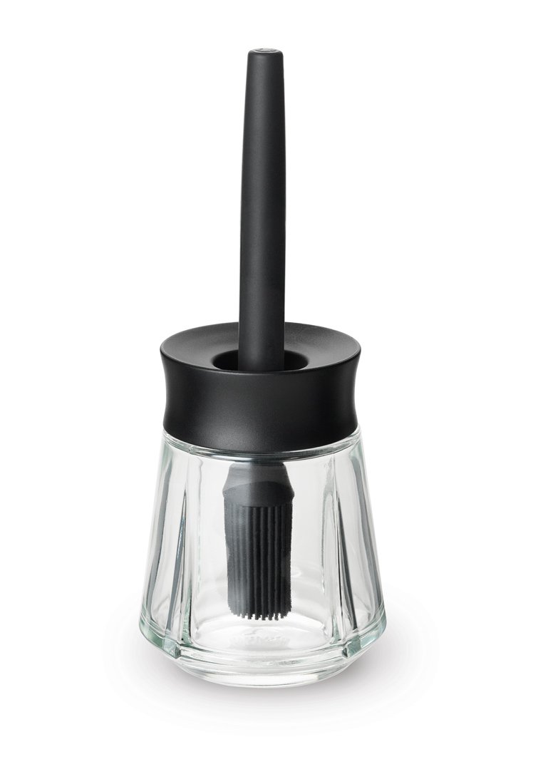 Klarer Glasbürstenhalter mit einer schwarzen Silikonbürste. Der Halter verfügt über einen zylindrischen Fuß mit einem flachen schwarzen Deckel und einem langen Griff.