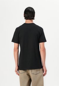 Mustast puuvillast lühikeste varrukatega T-särk, ümar kaelus, lõdvaistmeline ja sileda tekstuuriga; kantud heledate beežide pükstega, minimalistliku disainiga.