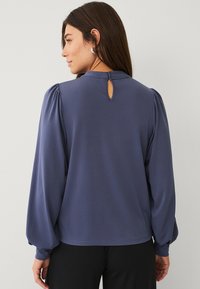 Marineblauwe blouse met gathered mouwdetails en een sleutelgatopening aan de achterkant. Gemaakt van lichtgewicht stof, heeft een losse, relaxte pasvorm.
