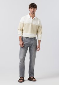 Polo met lange mouwen in een crème en beige kleurblok ontwerp, gecombineerd met grijze denim jeans en bruine instap sandalen. Glad materiaal, ontspannen pasvorm.