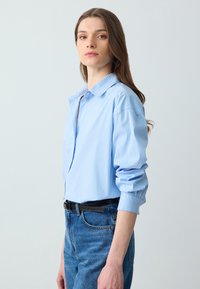 Lichtblauw gestreepte button-up shirt met een relaxte pasvorm, voorzien van een spits kraag en opgerolde mouwen, gecombineerd met hoge taille spijkerbroeken.