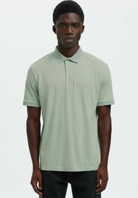 Svetlo zelena polo majica iz gladkega blaga, z klasičnim ovratnikom, dvema gumboma in kratkimi rokavi s teksturiranim poudarkom.