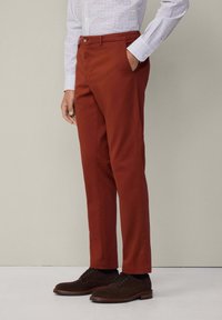 Slim-fit, verbrande oranje chinos van katoen, met zijzakken en een gladde textuur. Gecombineerd met donkerbruine suède schoenen.