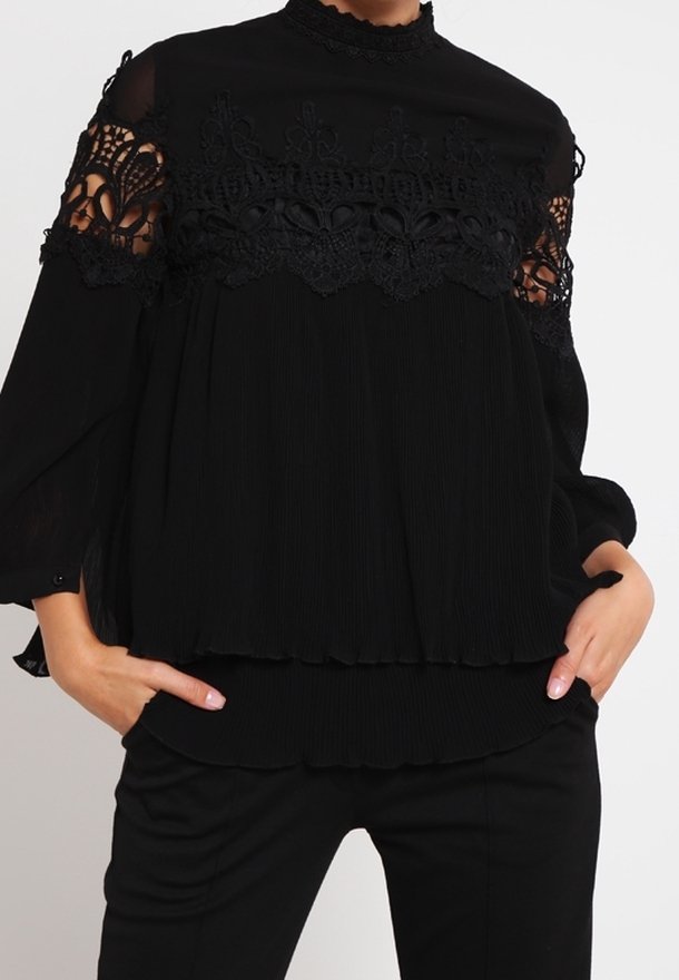 Czarna bluzka z wysokim dekoltem, bogato zdobiona koronką na przezroczystych rękawach i plisowanym materiałem z przodu, o luźnym kroju.
