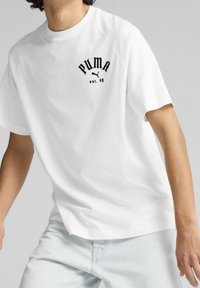 Camiseta de algodón blanca con un logo negro de Puma y el texto "est. 48" en el pecho, con un corte relajado y mangas raglán cortas.
