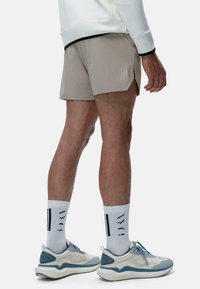 Beige athletic shorts with side slits, paired with light grey and blue sneakers, and white socks featuring black stripes.