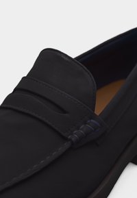 Mocassin en cuir noir avec détail de lanière penny et surpiqûres le long de l'avant et des côtés, incliné pour montrer l'avant et le côté.