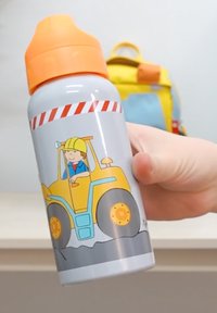 Die Hand eines Kindes hält eine Wasserflasche mit einem orangefarbenen Deckel, während im Hintergrund ein cartoonhafter Bauarbeiter in einem gelben Bagger fährt.
