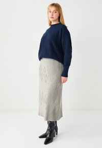 Marineblauer Pullover mit lockerem Schnitt, kombiniert mit einem grauen, gerippten, gemusterten Midirock und schwarzen kniehohen spitzen Stiefeln. Weiche Texturen und klare Linien.